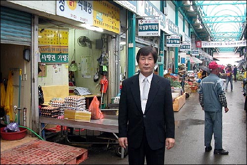 죽도시장 농산물거리의 백남도 회장. 백 회장의 왼쪽 뒤로 '사랑권 가맹점'이라고 쓴 안내문이 보인다. 